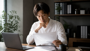 キャリアの選択肢を真剣に検討しながら資料とパソコンを見つめる日本人ビジネスパーソンのリアルな様子